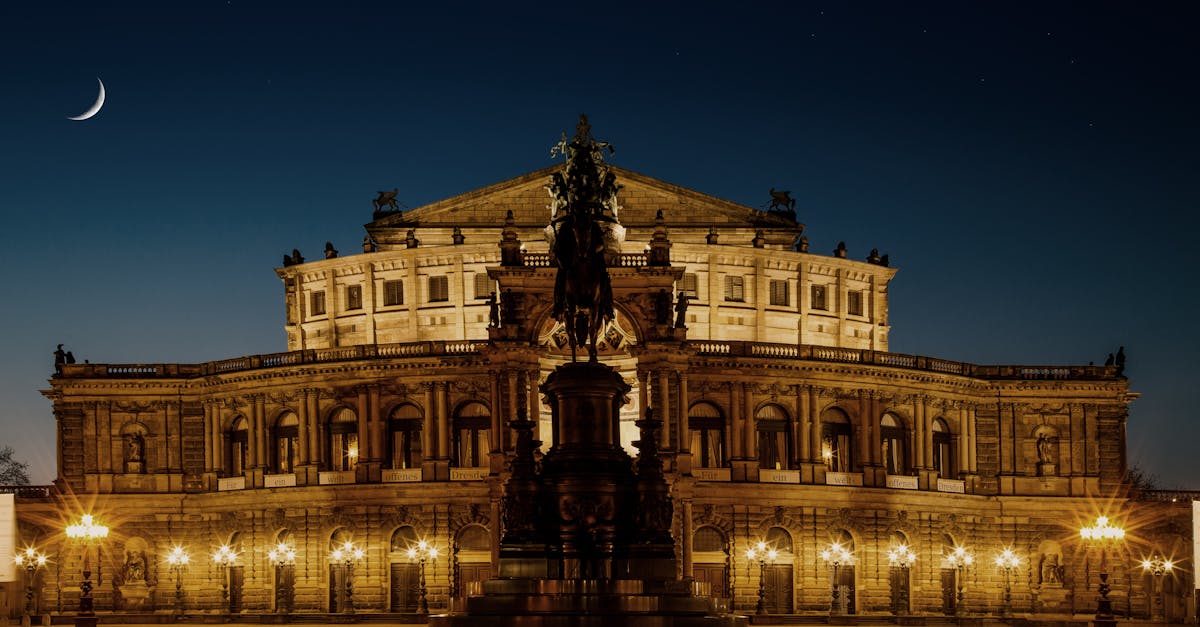Beautifully illuminated Semper Opera House in Dresden at night with a crescent moon in the sky.
