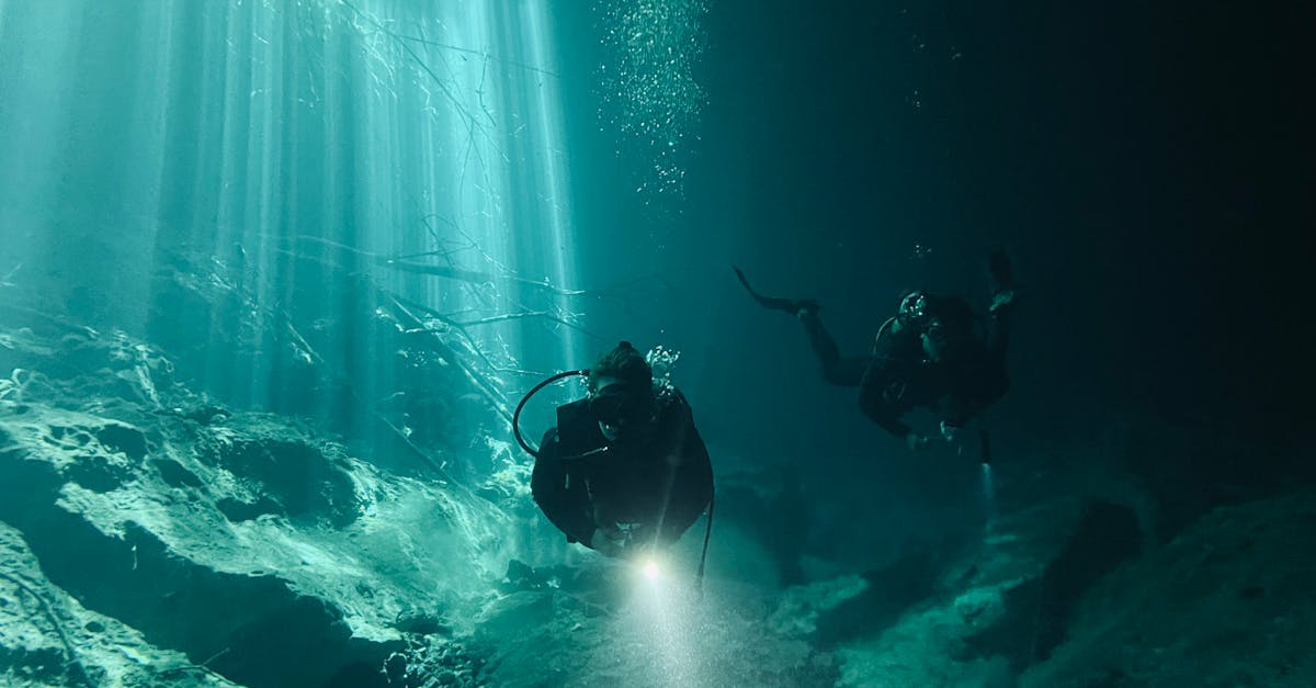 Scuba divers navigate underwater, exploring with flashlights and enjoying sunlight rays.