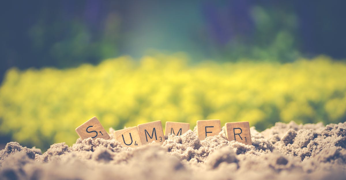 Scrabble tiles forming the word 'summer' in sand with a blurred background, evoking warm vibes.