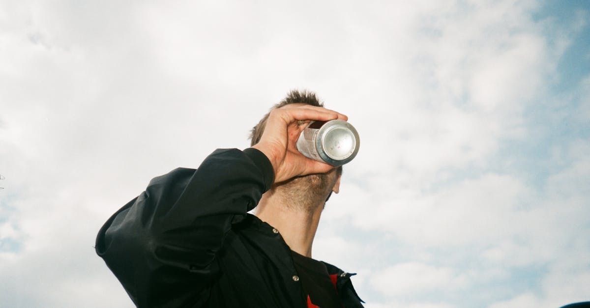 Low angle view of a man drinking from a can against a blue sky with clouds.