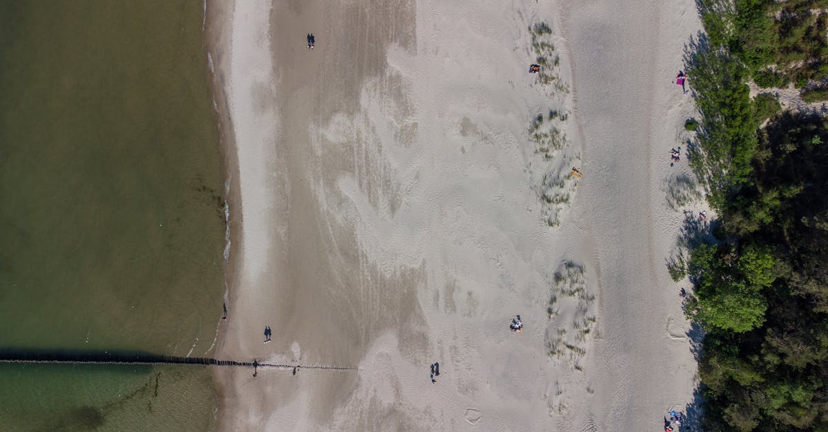 Bird's eye view of a sandy beach and shoreline in Ustka, Poland, with people walking.