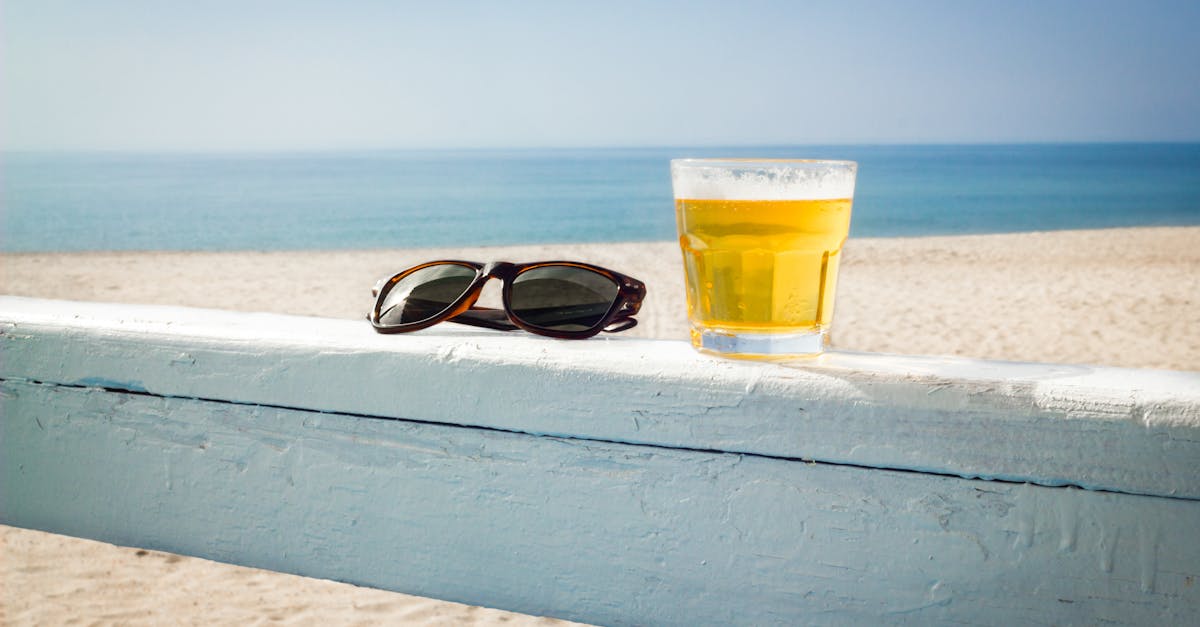 A chilled glass of beer and sunglasses on a beach railing. Perfect summer vibes.