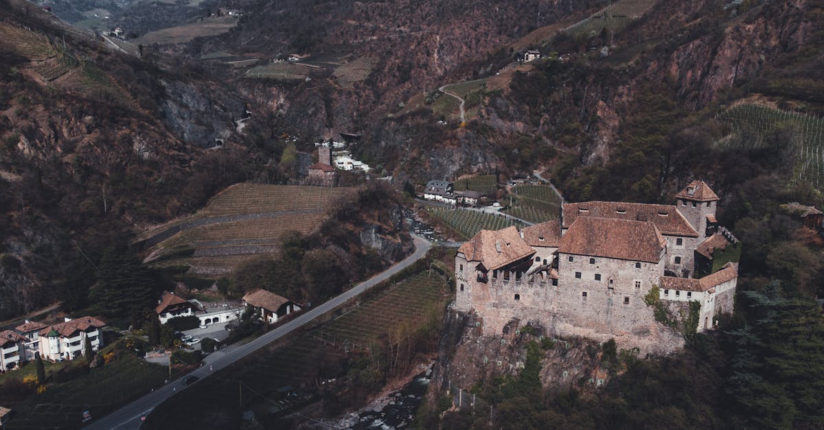 Aerial view of a medieval castle surrounded by vineyards and mountains in Bolzano, Italy.