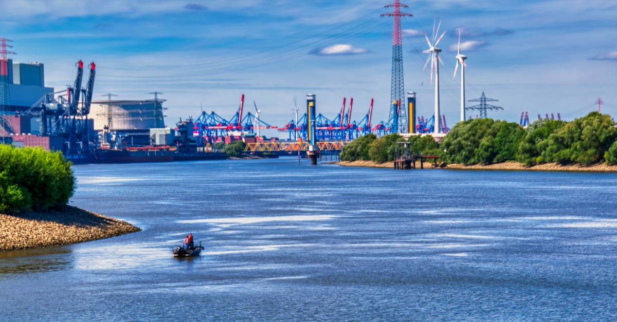 Picturesque view of a river and industrial area with wind turbines and a small boat under a blue sky.