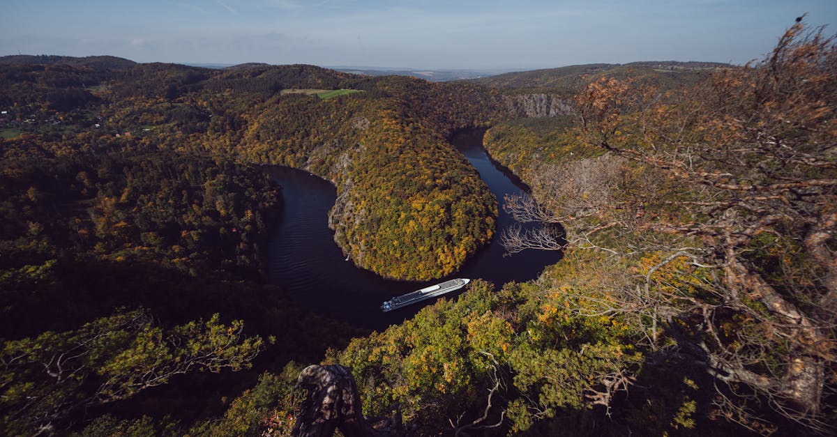 A captivating aerial view of the Vltava River winding through autumn foliaged mountains in Czechia.