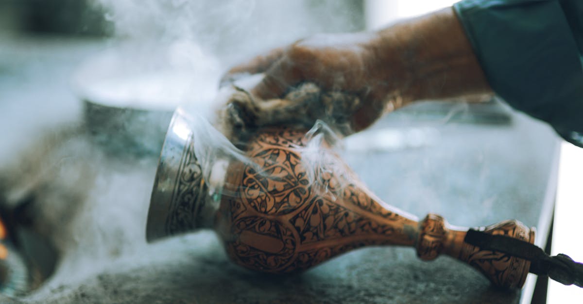 Close-up of an artisan's hand crafting a smoking decorative vase with intricate designs.