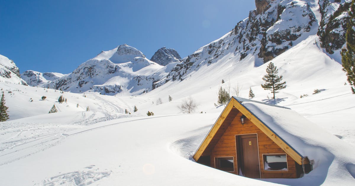 Wooden cabin amidst snowy mountains under a clear blue sky.