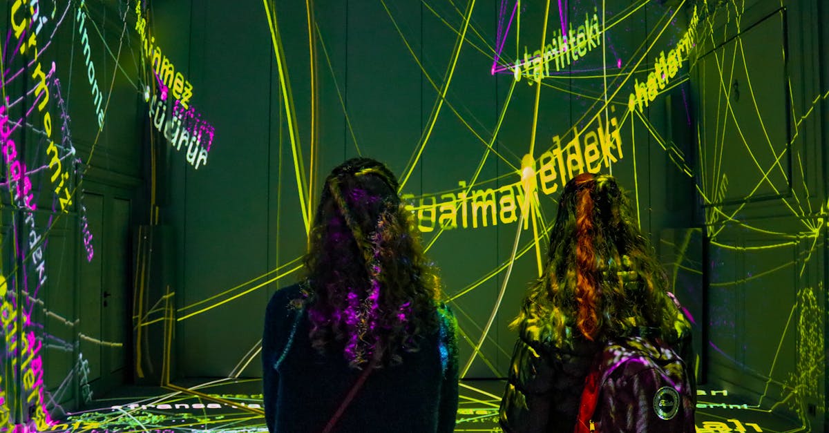Two women observe a dynamic text projection art installation in a dark room.