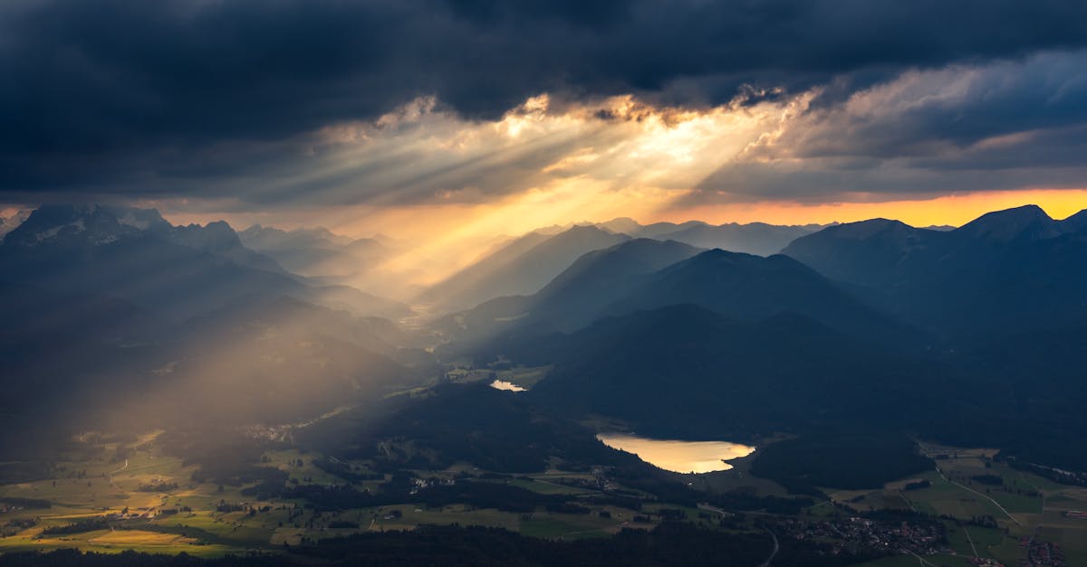 Sunbeams piercing through clouds over a scenic mountain and valley landscape at sunset.