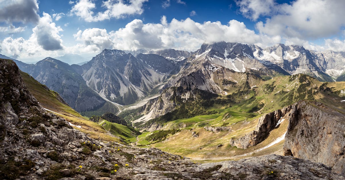 Stunning alpine landscape with towering peaks and vibrant green valleys under dramatic clouds.