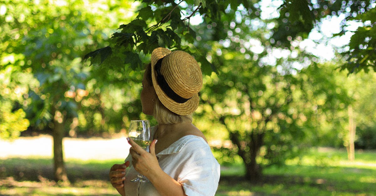 A woman in a straw hat holding a wineglass, enjoying a sunny day in a green park.