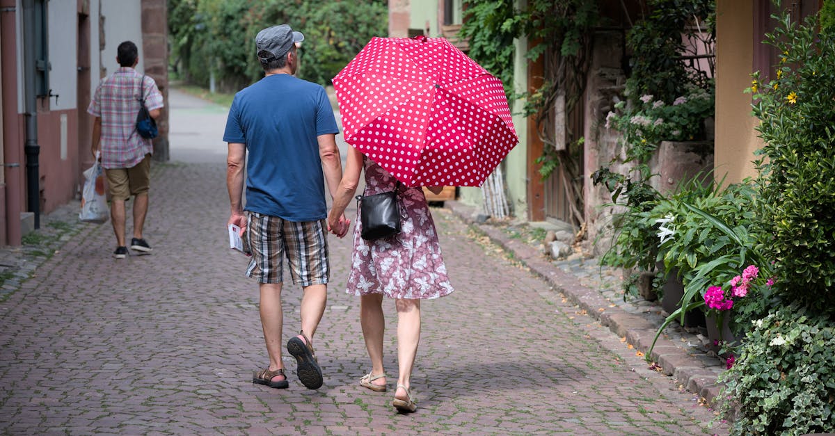 Couple walking under a red polka-dot umbrella on a cobblestone street in Kaysersberg, France.
