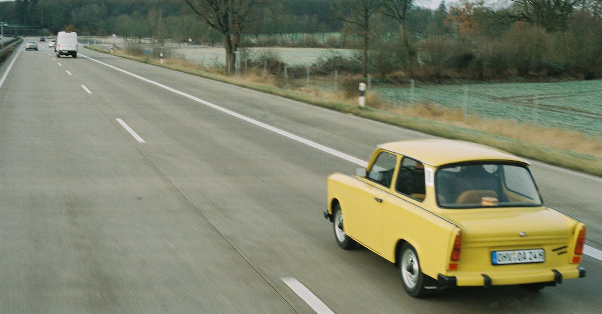 A classic yellow Trabant driving on a quiet highway with sparse traffic.