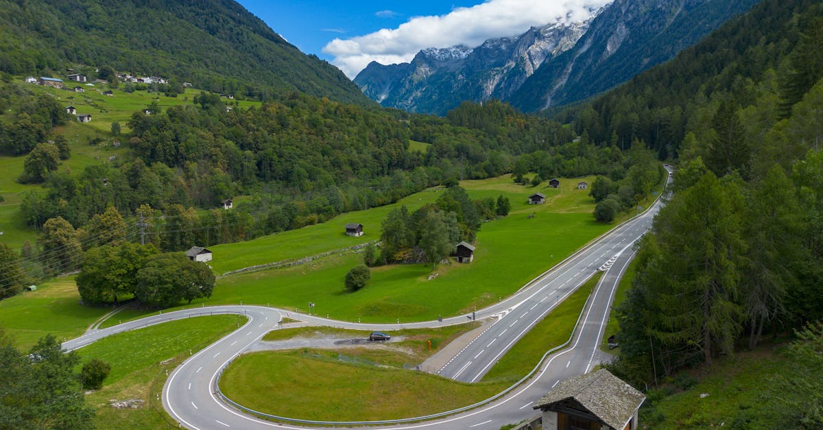 A winding road cuts through the lush green valley of Bregaglia, Switzerland with mountain views.