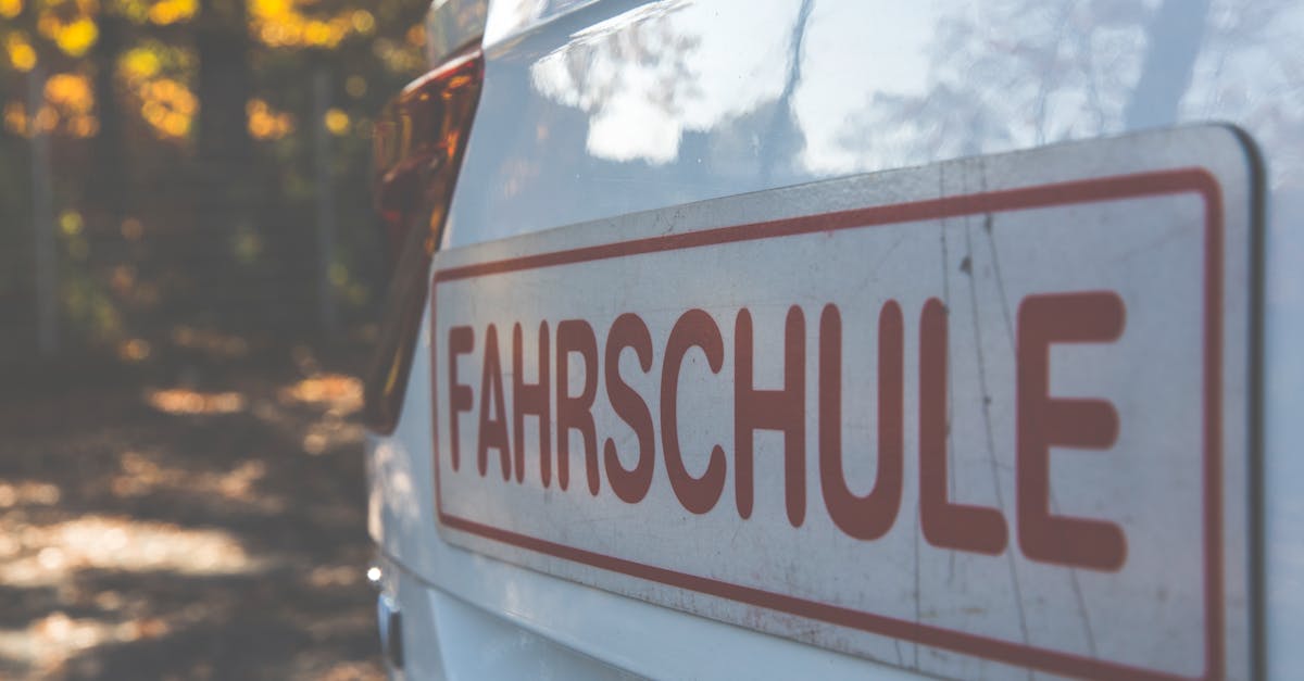 A side view of a white car with a Fahrschule sign, outdoors with autumn foliage.