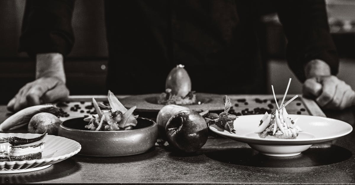 Chef arranges gourmet dishes on a table in a black and white setting.