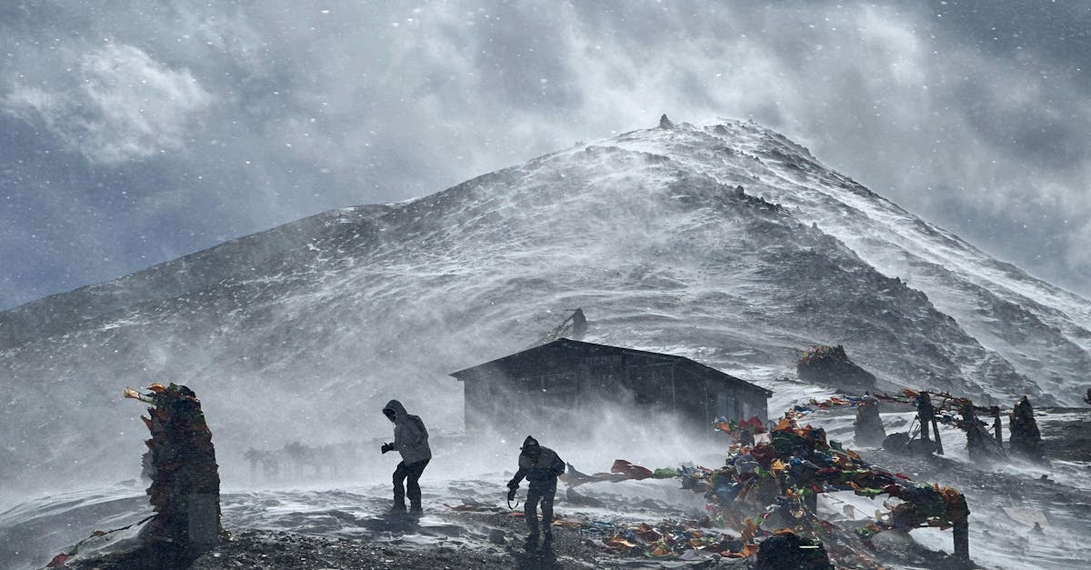 Adventurers facing harsh winds and snow on a rugged mountain path during winter.