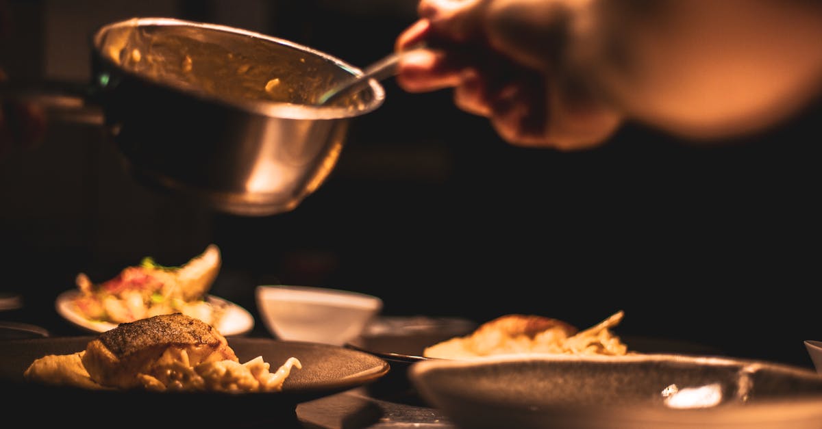 Gourmet dish being plated by a chef in a dimly lit restaurant's kitchen.