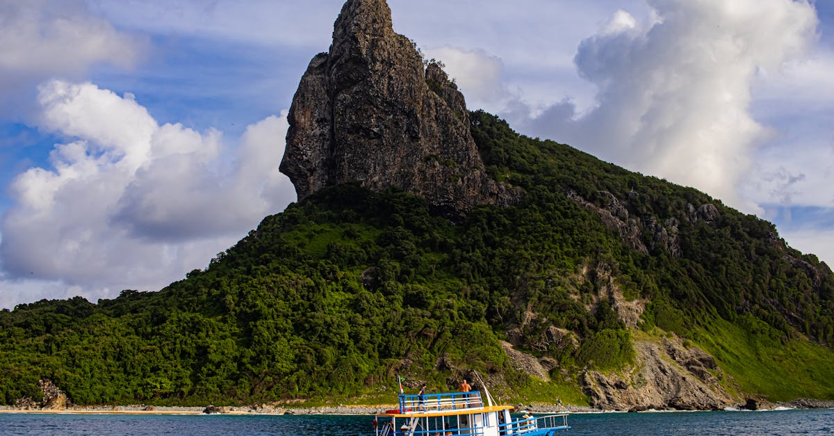 A vibrant boat sails by a stunning rocky island with lush greenery under a dramatic sky.