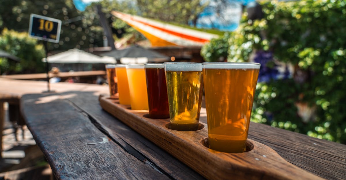 A vibrant beer flight displayed on a rustic wood table outdoors during a sunny day.