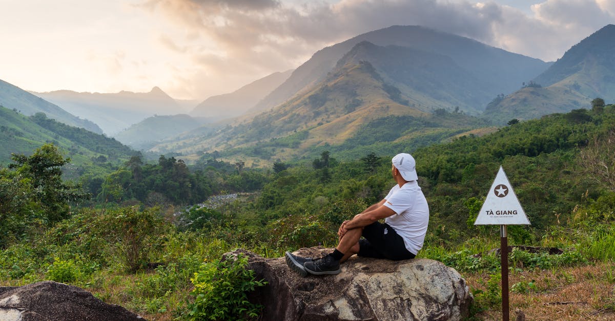 Man sitting on rock admiring scenic Tà Giang mountain view at dawn.
