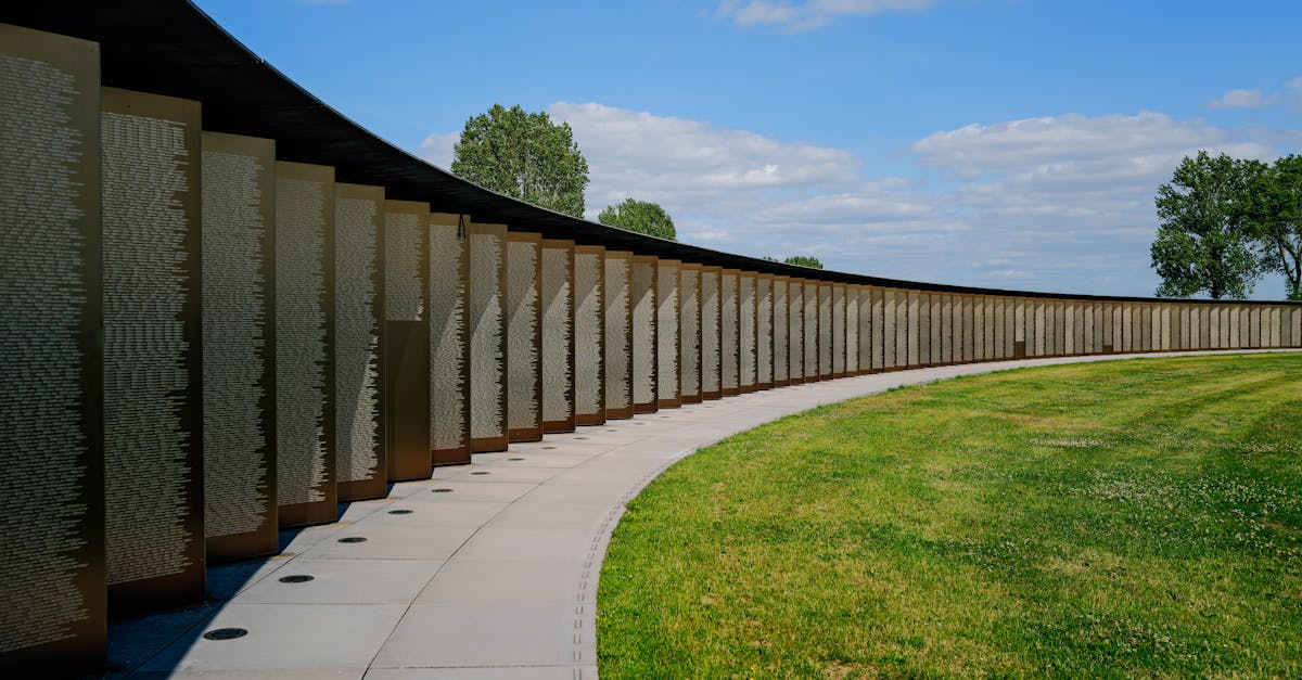 A curved memorial wall under a clear blue sky in a sunlit park with grassy surroundings.