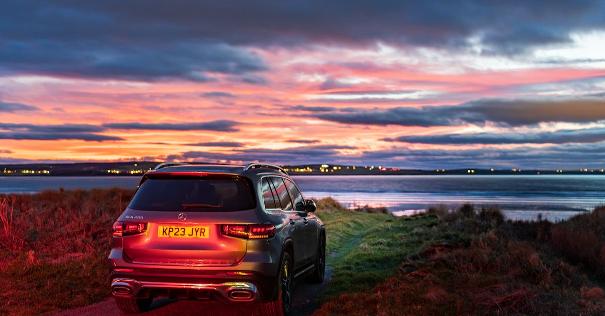 A modern SUV parked by a lake during a vibrant sunset, showcasing a scenic landscape.