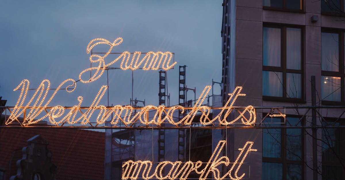 Glistening Christmas market sign lights up the evening sky in a city center, creating a warm festive ambiance.