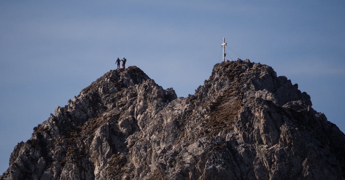 Two hikers stand on a rocky mountain peak next to a cross under a clear blue sky in Innsbruck, Austria.