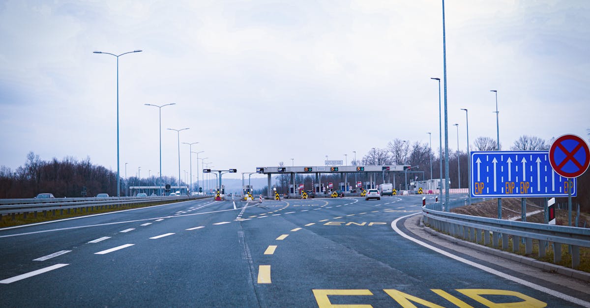 Wide highway leading to a toll plaza under a cloudy sky, featuring road signs and empty lanes.