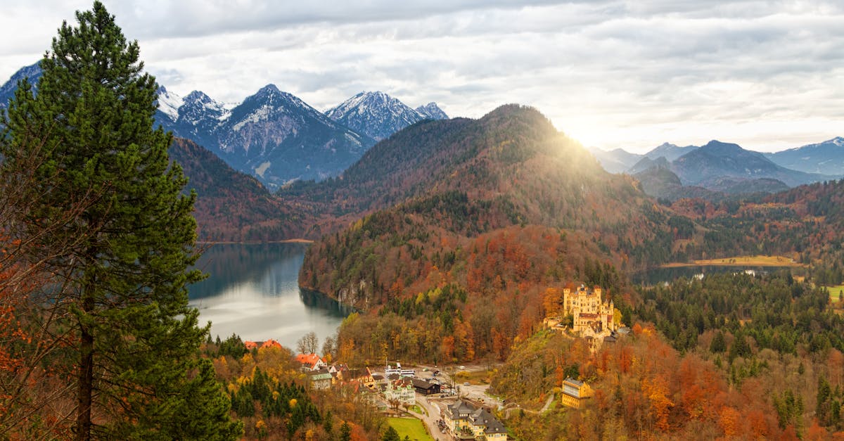 Stunning autumn view of Hohenschwangau Castle amid mountains, lake, and forest.