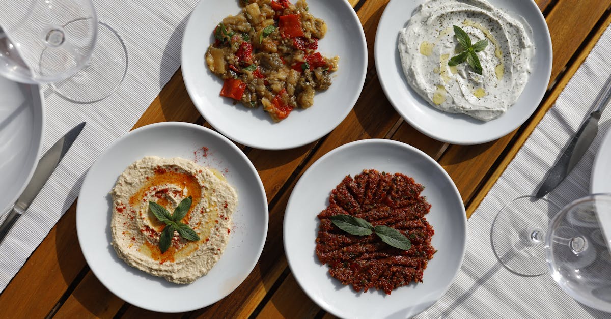 Aerial view of Mediterranean meze with diverse dips on white plates, outdoors.