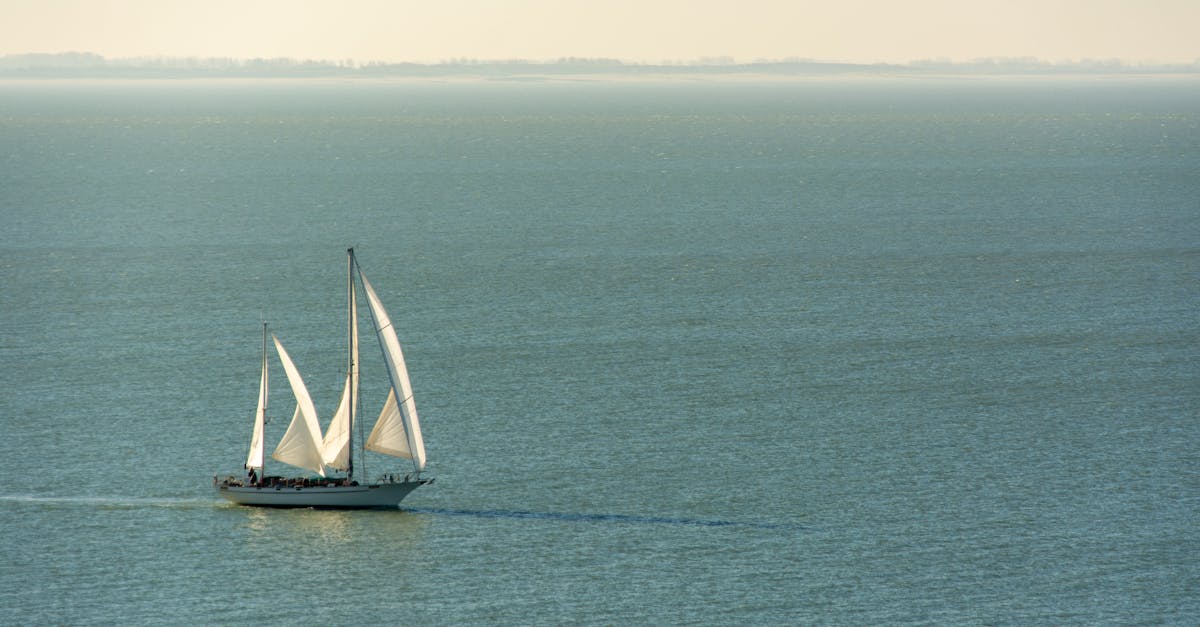 Peaceful scene of a large sailing ship with white sails on a tranquil sea during the day.