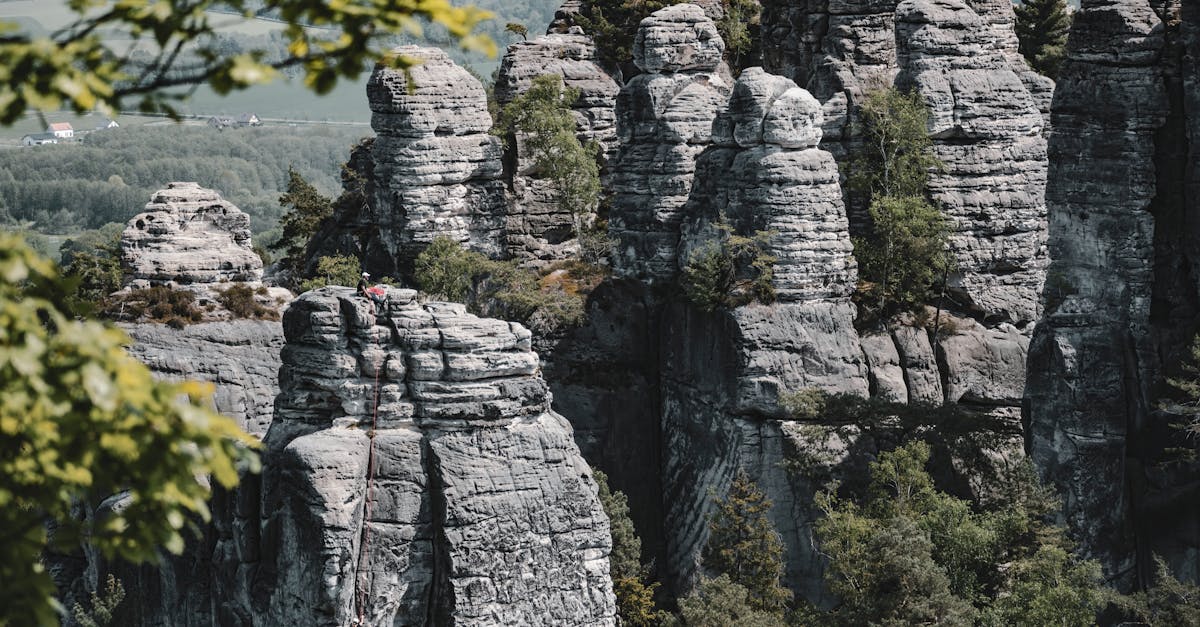 Adventurous climbers scale towering sandstone formations in Česko, surrounded by lush forests and open landscapes.