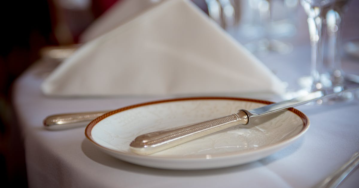 Close-up of a formal table setting with silverware, a plate, and a folded napkin on a white tablecloth.