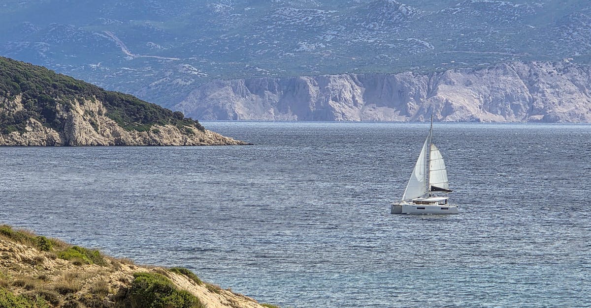 A serene coastal landscape with a sailing boat and distant mountain views.