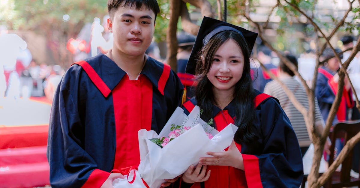 Two graduates in cap and gown celebrating outdoors, holding a bouquet.
