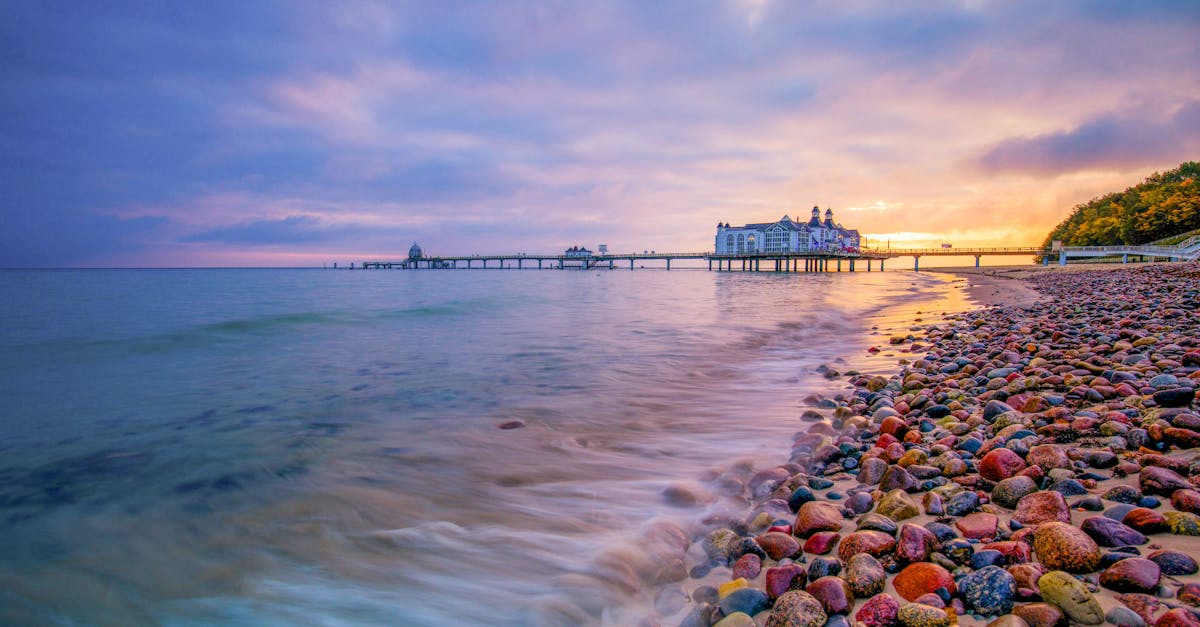 Vibrant beach sunset with a pier and colorful pebbles along the shore, creating a serene atmosphere.