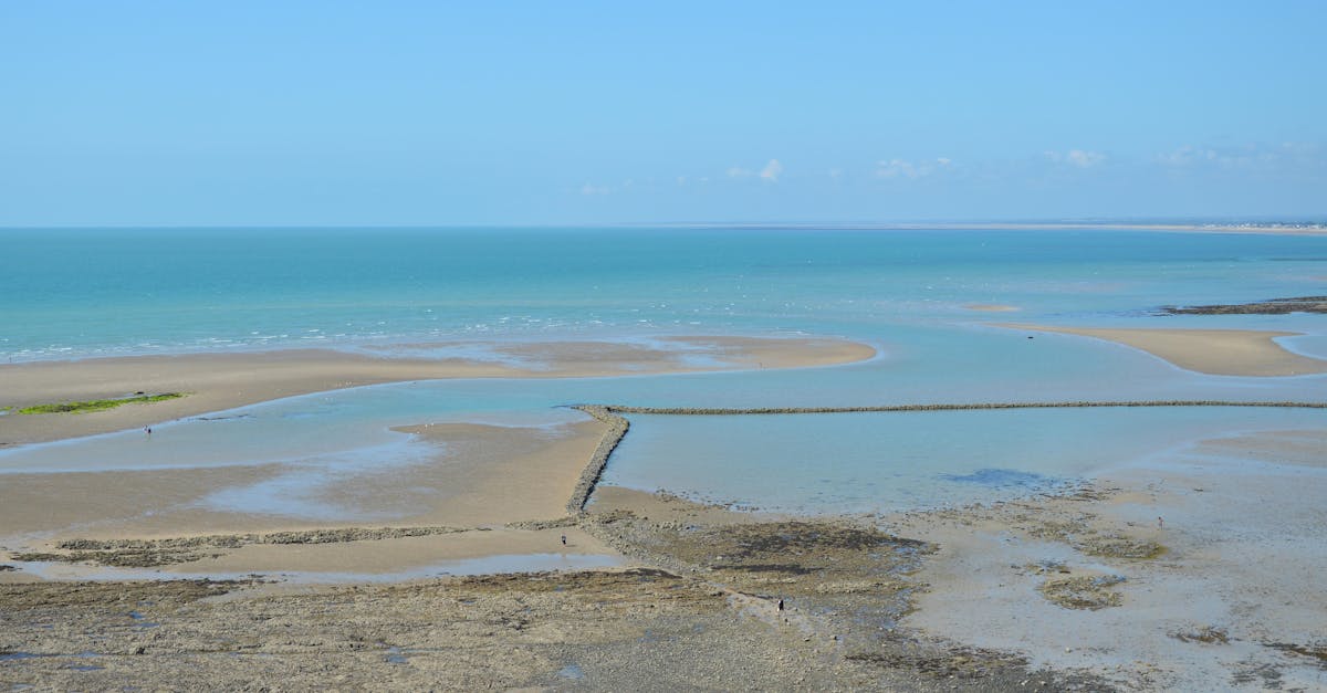 A serene view of Granville beach in Normandie, France, with tidal pools and clear blue skies.