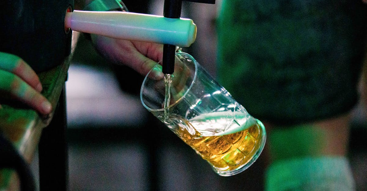 Close-up of a person pouring beer from a tap into a glass at a bar.