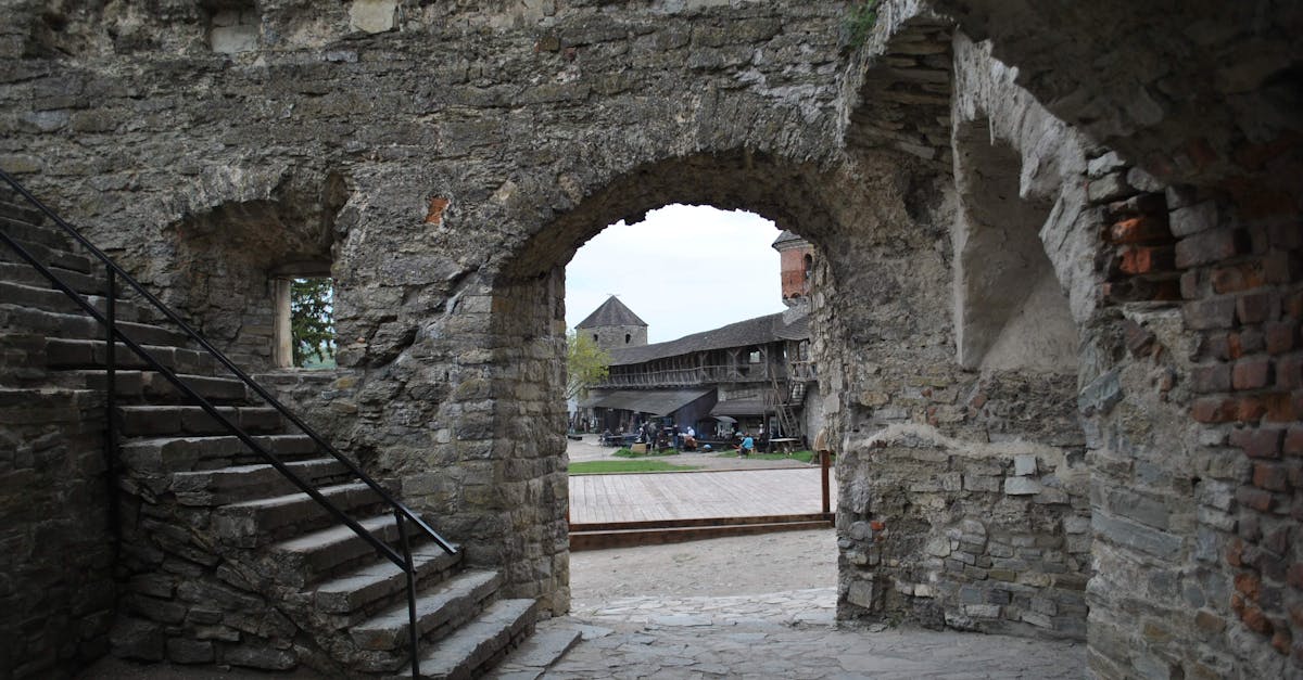 A view through a stone archway of a historic courtyard with a staircase and ancient walls, depicting medieval architecture.