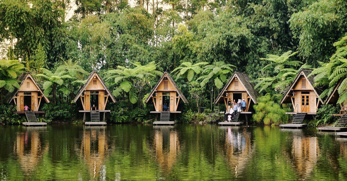 Picturesque wooden cabins reflect over a tranquil lake against lush greenery.