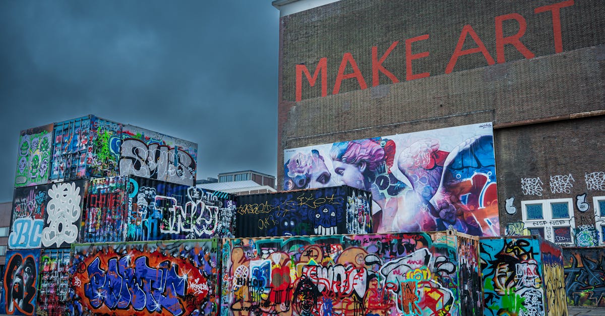 Vibrant graffiti art decorates shipping containers and a building wall with 'MAKE ART' text under a dramatic sky.