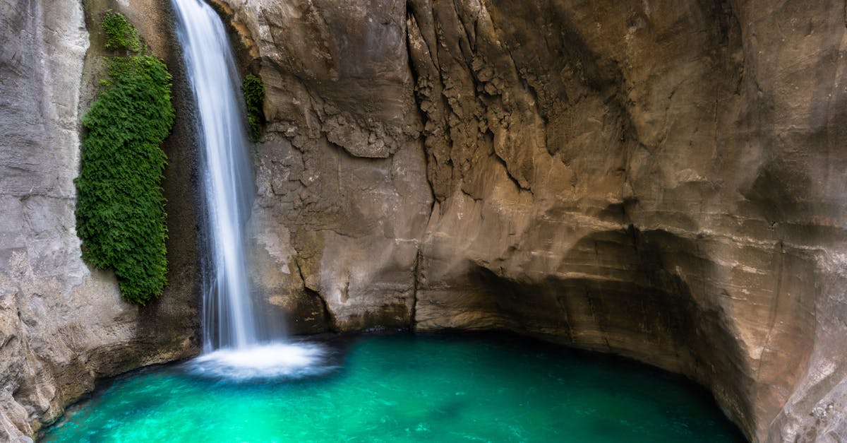 A beautiful waterfall flows into an emerald pool inside a rocky cave, creating a serene natural scene.