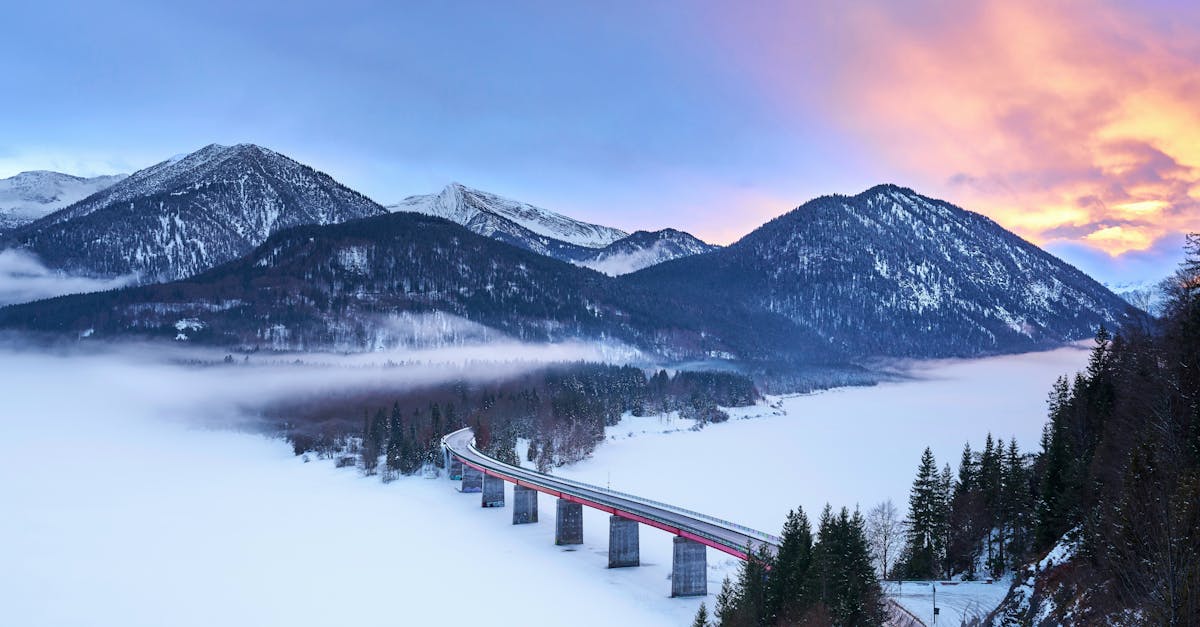 Stunning view of a bridge in the snow-covered Bavarian Alps at sunrise, showcasing serene winter beauty.