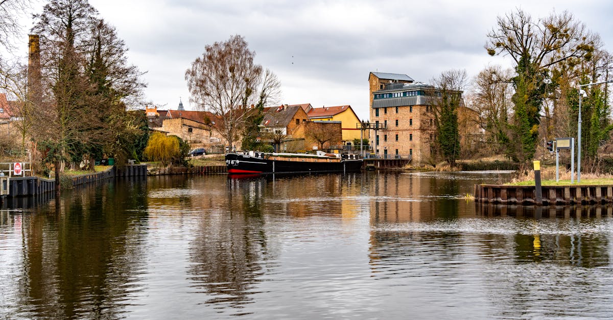 Scenic view of a serene river with a boat and charming village, reflecting autumn trees and quiet water.