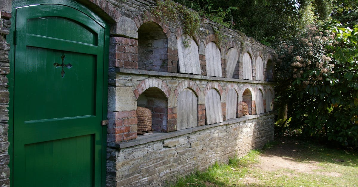 A traditional stone bee house with green door in a garden setting under clear skies.