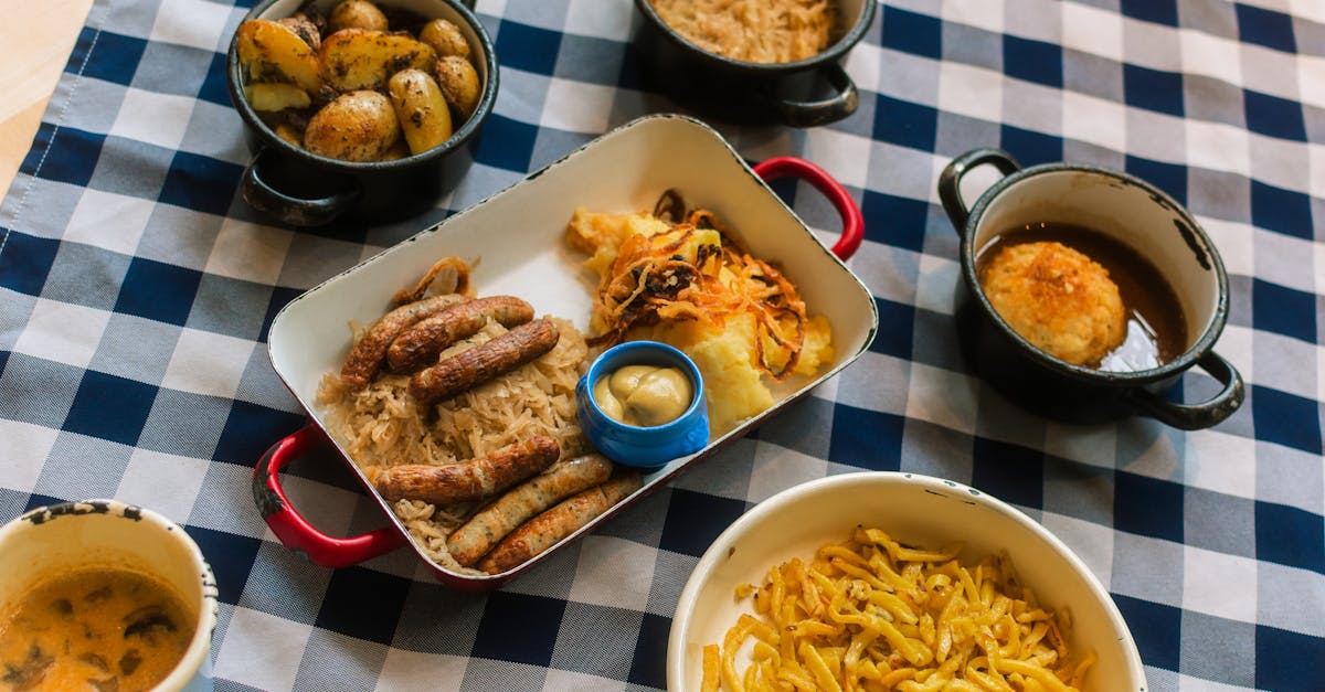 Traditional Bavarian meal featuring sausages, potatoes, cabbage, and mustard served on a checkered tablecloth.