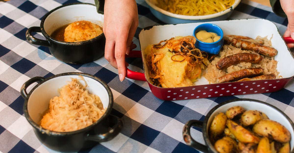 Traditional Bavarian meal with sausage, sauerkraut, potatoes, and gravy on a checkered tablecloth.