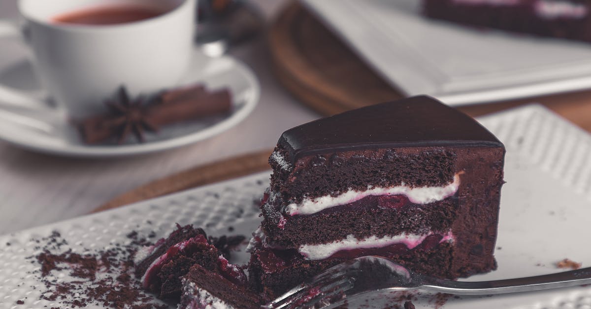 Closeup of a rich chocolate cake slice on a plate with a tea cup in the background.